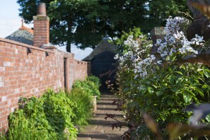 A brick pathway leading to a building with a tiled roof, surrounded by lush greenery and flowering plants. - Piersland House (Troon)
