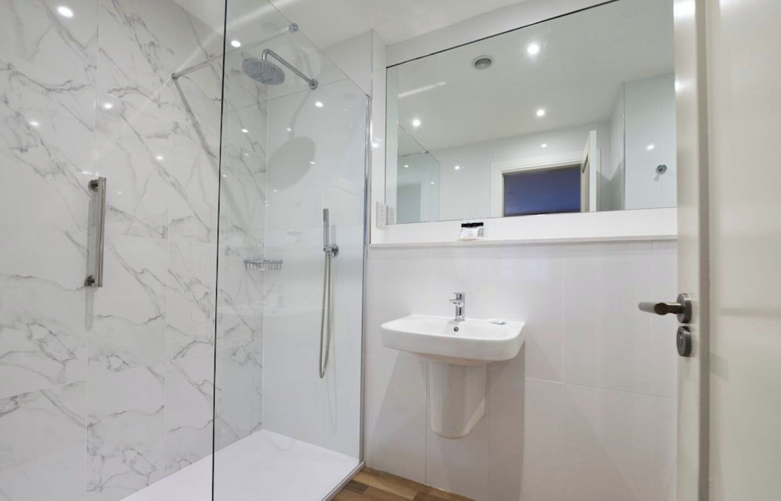 A modern bathroom with a glass-enclosed shower, a white sink, and a mirror above the sink.