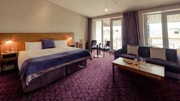A hotel room with a large bed, a sofa, a coffee table, and a balcony with a view.
