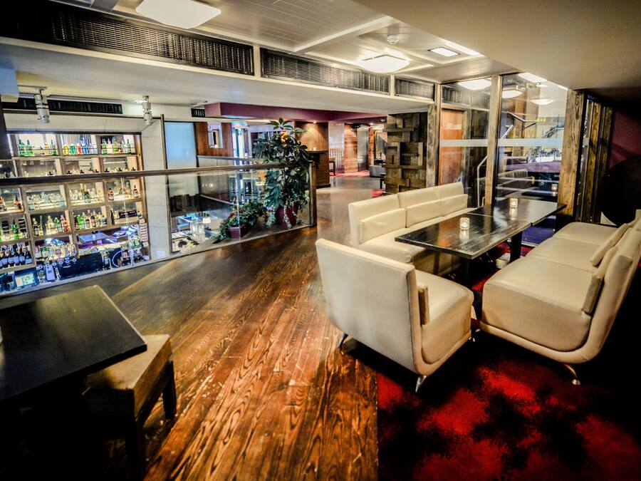A bar area with a wooden floor, white seating, and a glass enclosure displaying bottles.