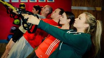 Un grupo de personas ejercitándose con correas TRX en una sala con paredes rojas y pelotas de ejercicio.