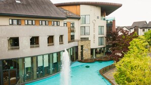 Un hotel con piscina central que incluye una fuente, amplios ventanales de vidrio y fachada de piedra.