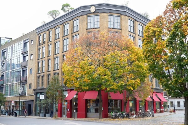 A multi-story building with a red awning and a tree with autumn leaves in front.