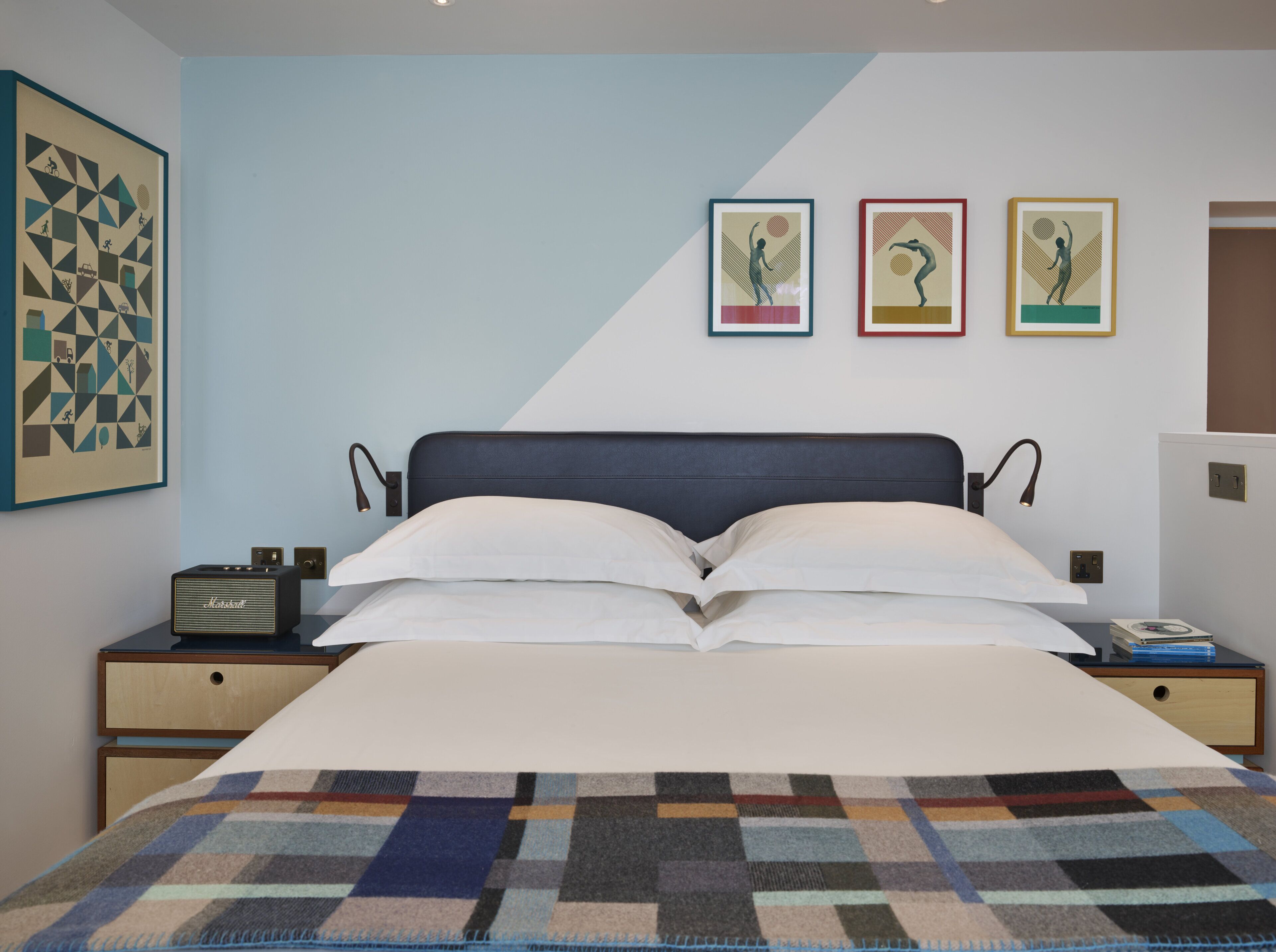 Un dormitorio moderno con cama, mesitas de noche, una radio y tres obras de arte enmarcadas en la pared.