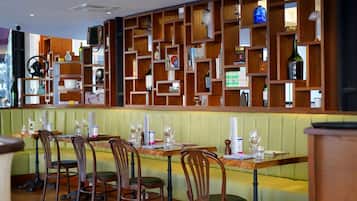 Un restaurante con estantes de madera que exhiben diversos objetos, asientos tapizados en verde y sillas de madera.