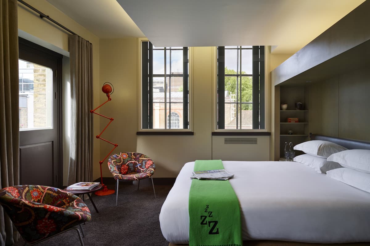 A hotel room with a bed, a chair, a desk, and a window.