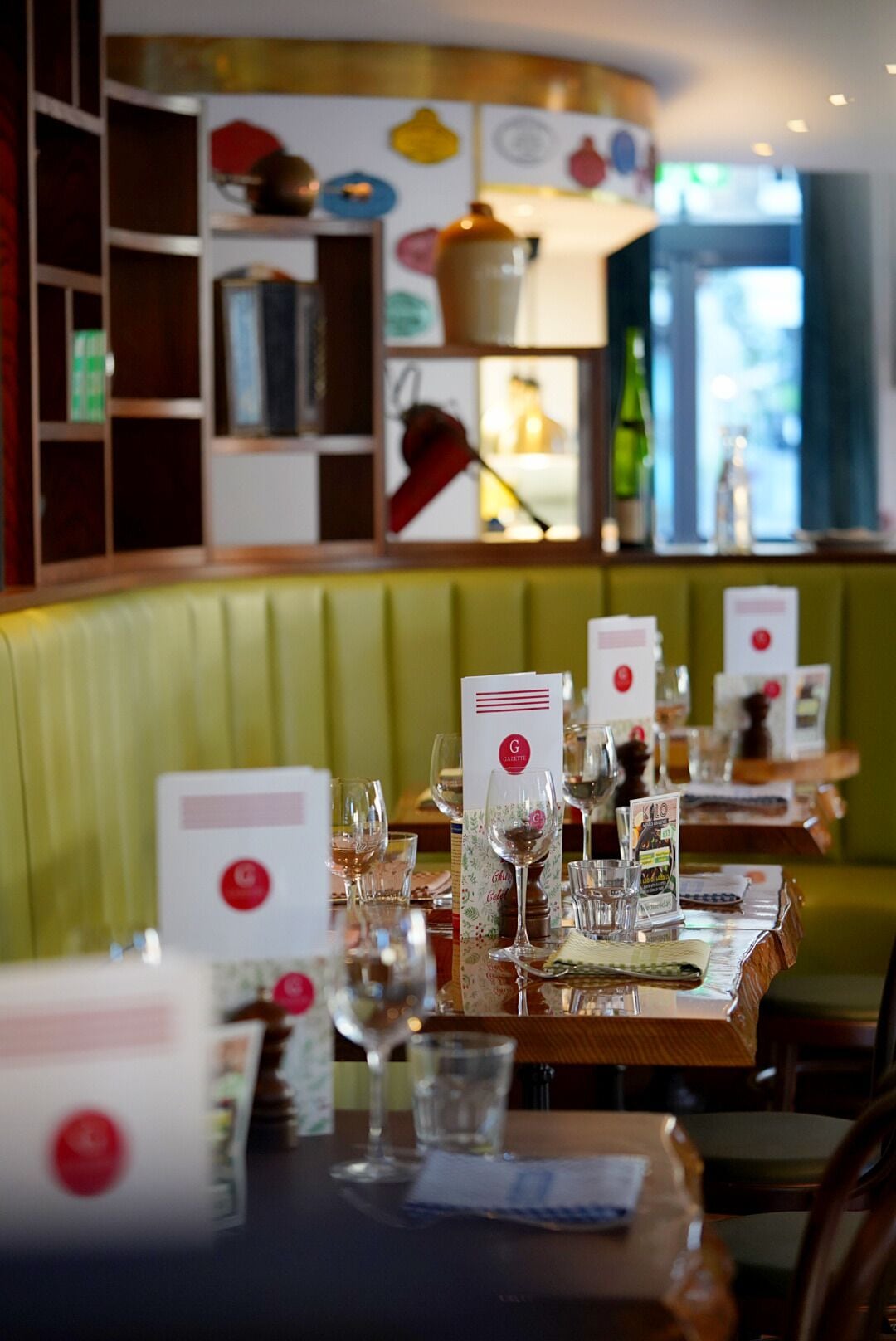 Un interior de restaurante con cabinas, mesas dispuestas con copas de vino, menús y una pared acolchada de color verde.