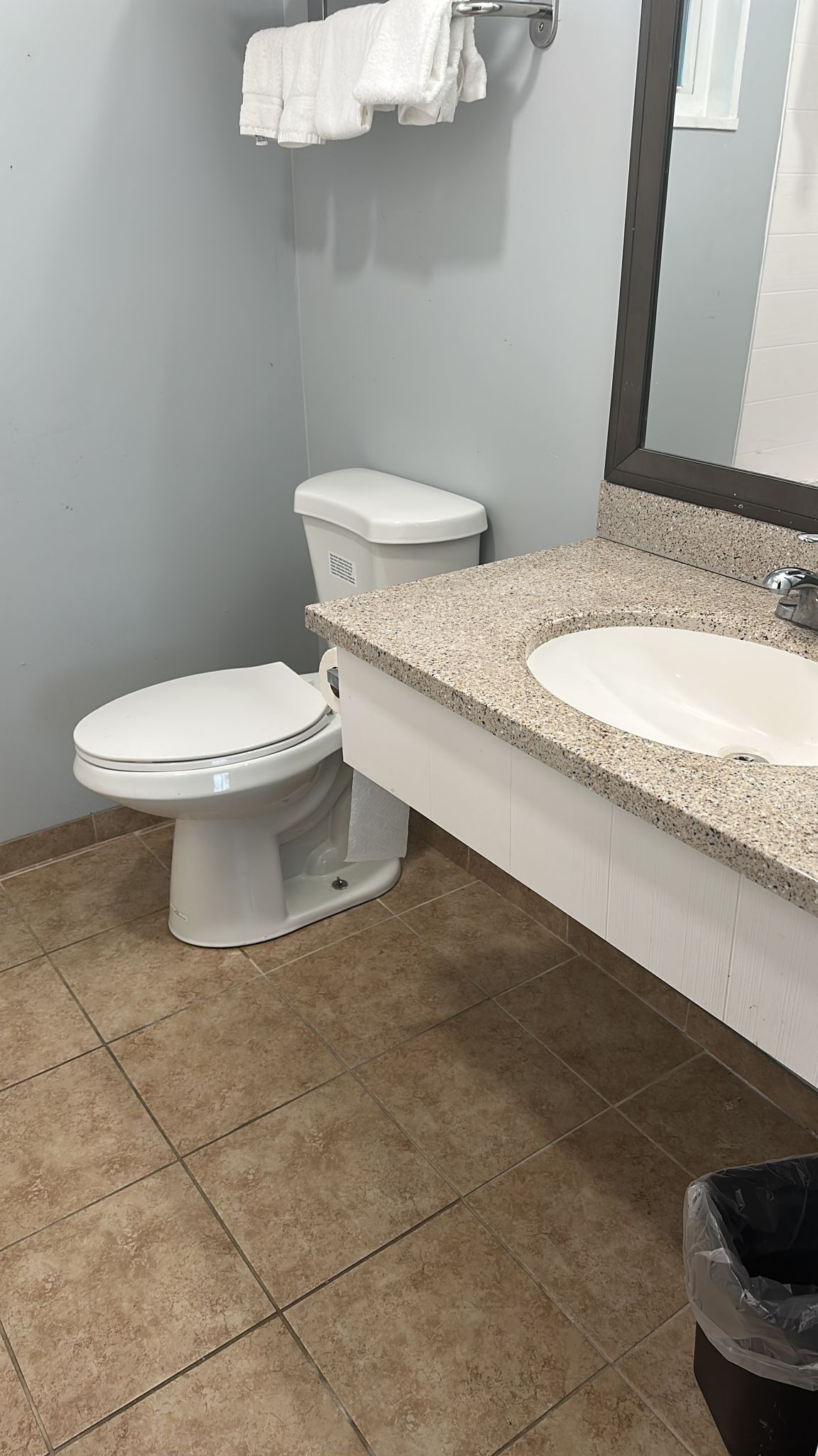 Une salle de bain avec des toilettes blanches, un lavabo doté d’un plan de travail en granit et un miroir au-dessus du lavabo.