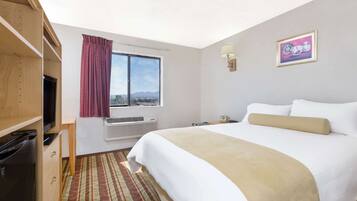Habitación de hotel con cama, televisor, ventana con cortinas, luz empotrada en la pared y un cuadro enmarcado.