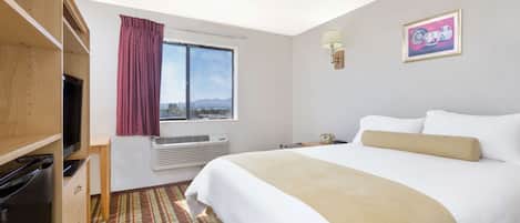 Habitación de hotel con cama, televisor, ventana con cortinas, luz empotrada en la pared y un cuadro enmarcado.
