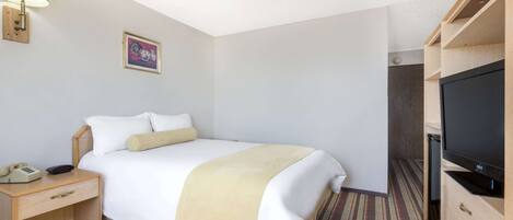 Habitación de hotel con cama, mesita de noche con lámpara, televisor y un cuadro en la pared.