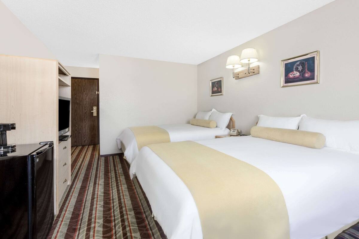 Une chambre d’hôtel avec deux lits, un bureau, une chaise, une lampe et un tableau au mur.