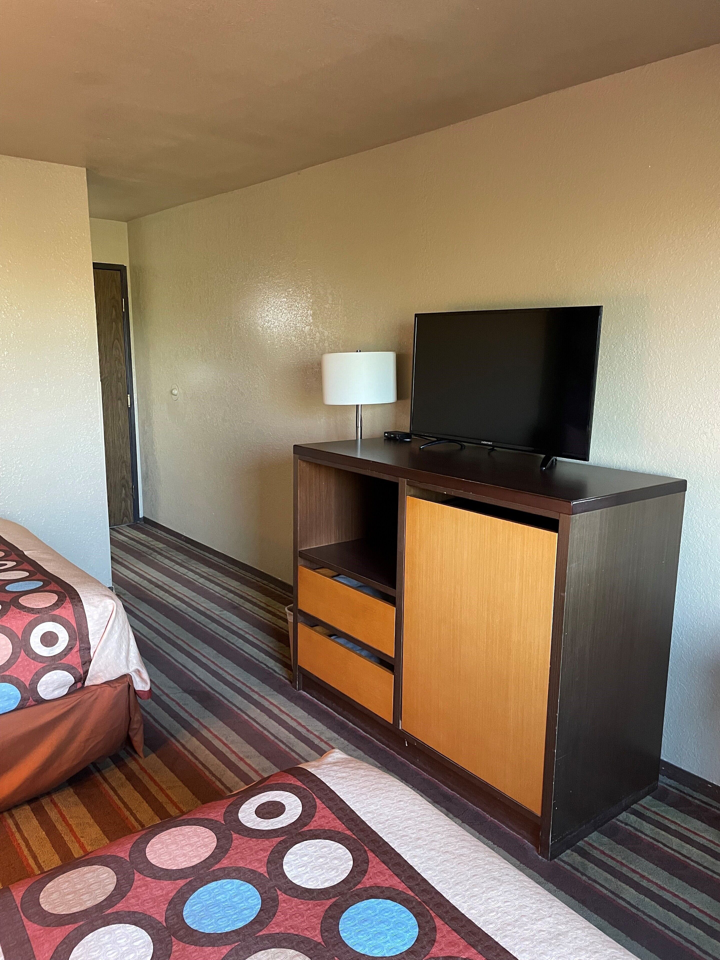 Une chambre d’hôtel avec un lit, un téléviseur posé sur une commode en bois et un tapis à motifs.