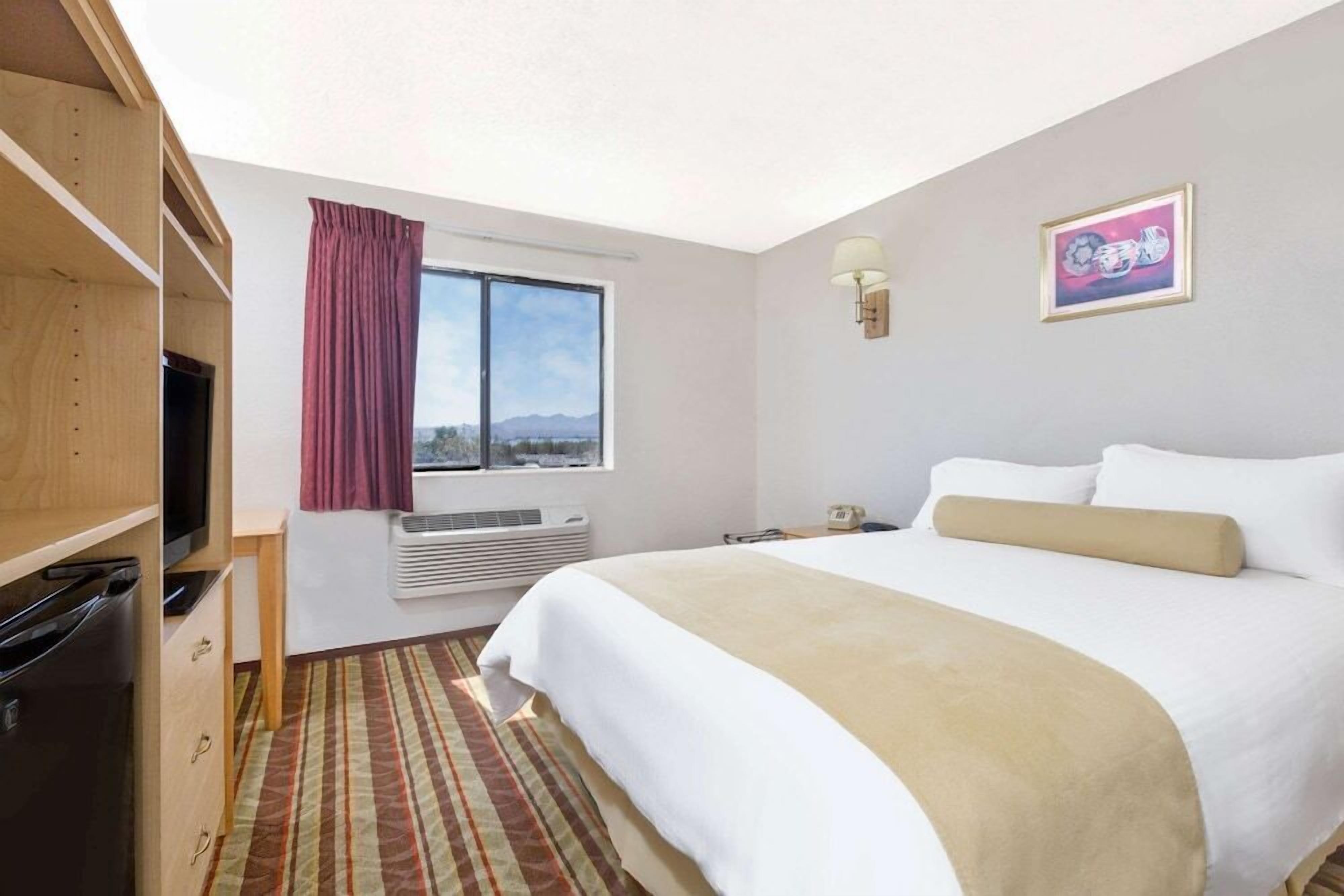 Quarto de hotel com cama, televisão, janela com cortinas, aquecedor e quadro na parede.