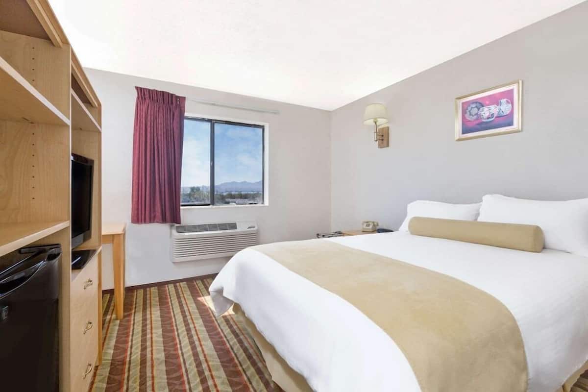 Une chambre d’hôtel avec un lit, une télévision, une fenêtre avec des rideaux, un radiateur et un tableau encadré au mur.