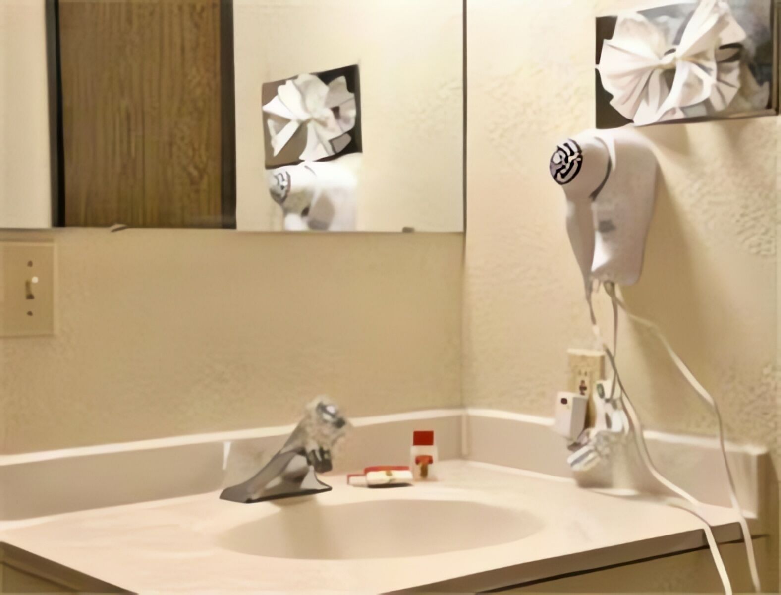 A bathroom with a sink, mirror, and hairdryer mounted on the wall.