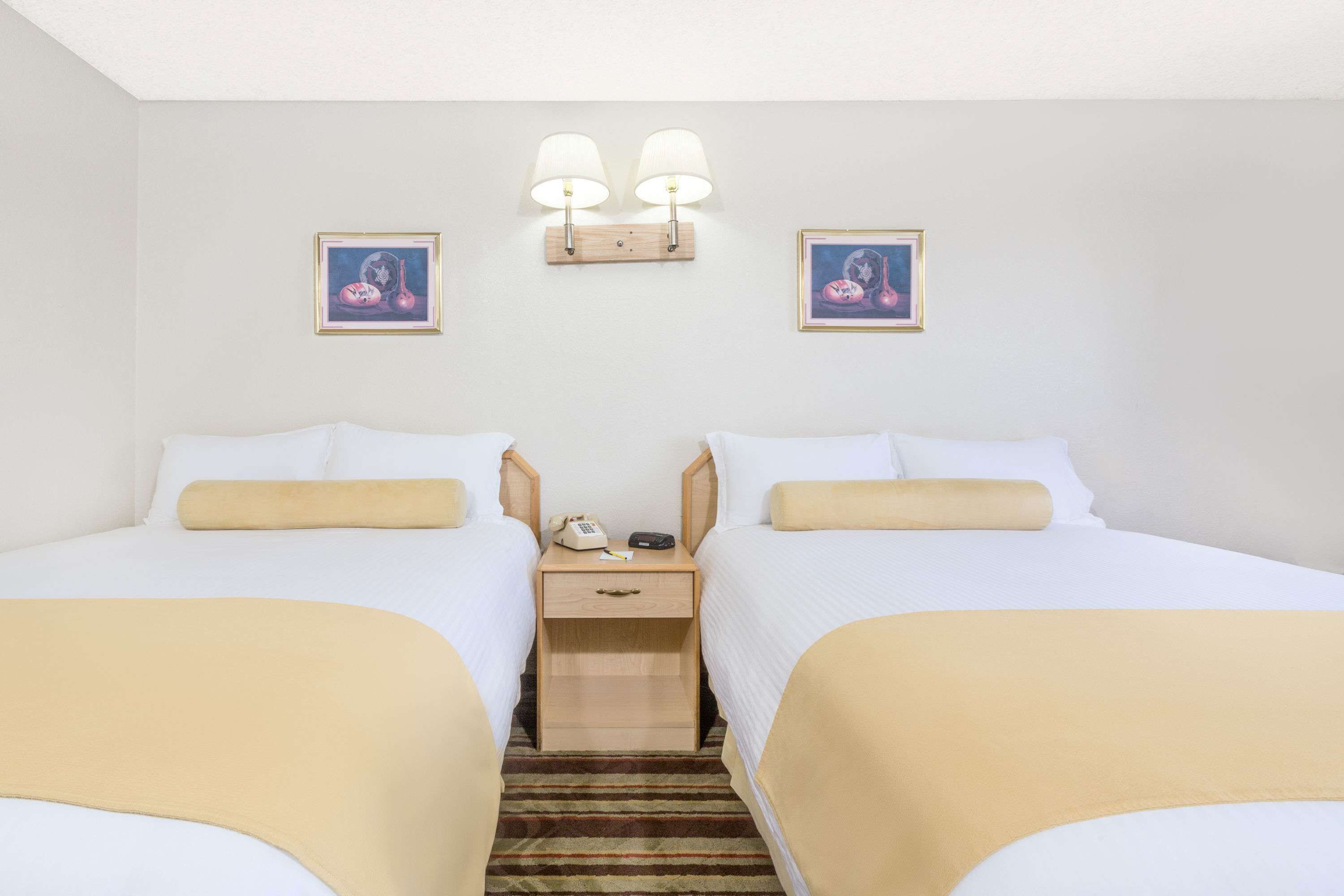 A hotel room with two beds, a nightstand with a phone and lamp, and two wall-mounted lamps.