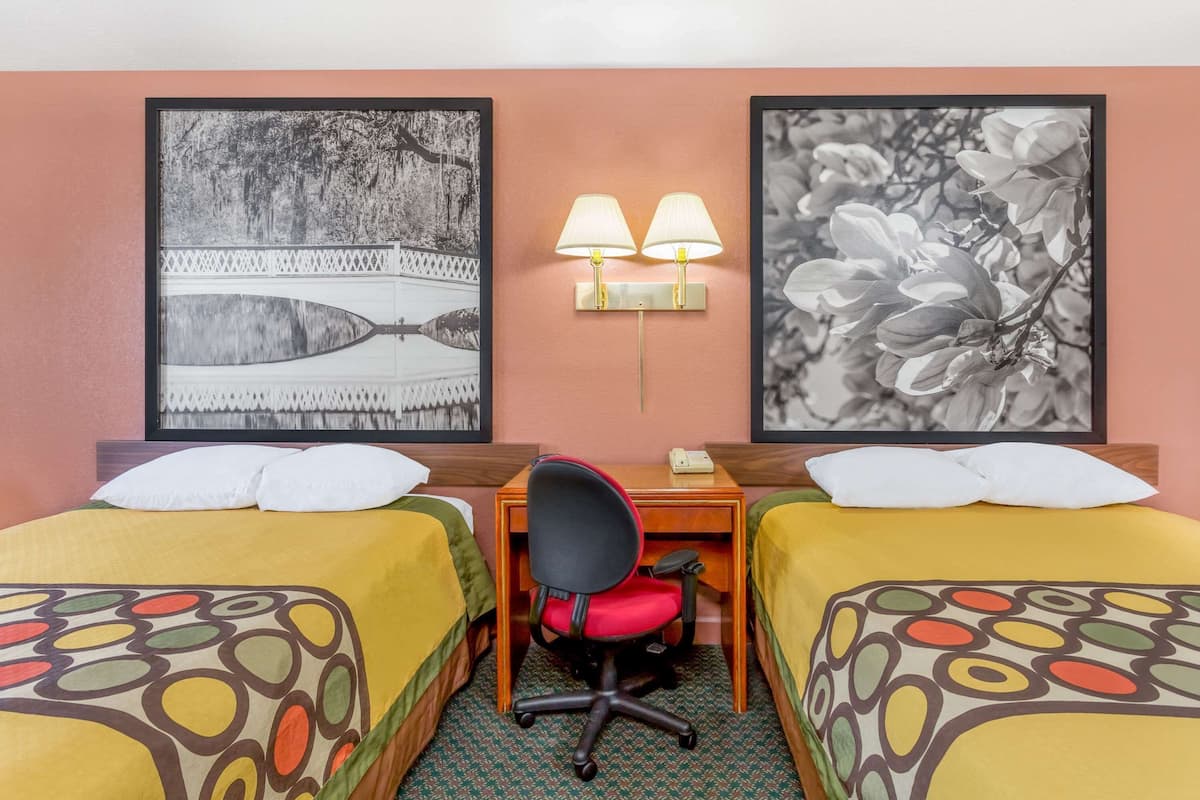 Une chambre d’hôtel avec deux lits, un bureau avec une chaise et deux lampes fixées au mur.