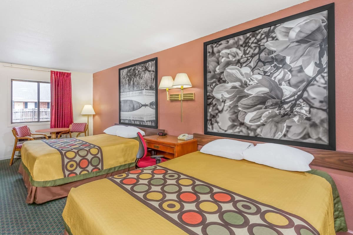 Une chambre d’hôtel avec deux lits, un bureau, une chaise, une lampe et une fenêtre avec des rideaux.