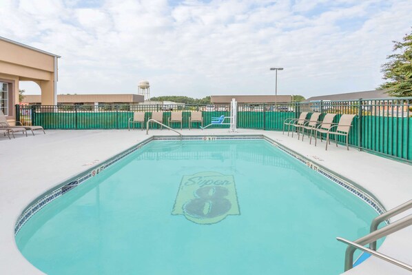 Una piscina con el logotipo de Super 8, rodeada de vallas verdes y sillas reclinables color beige.