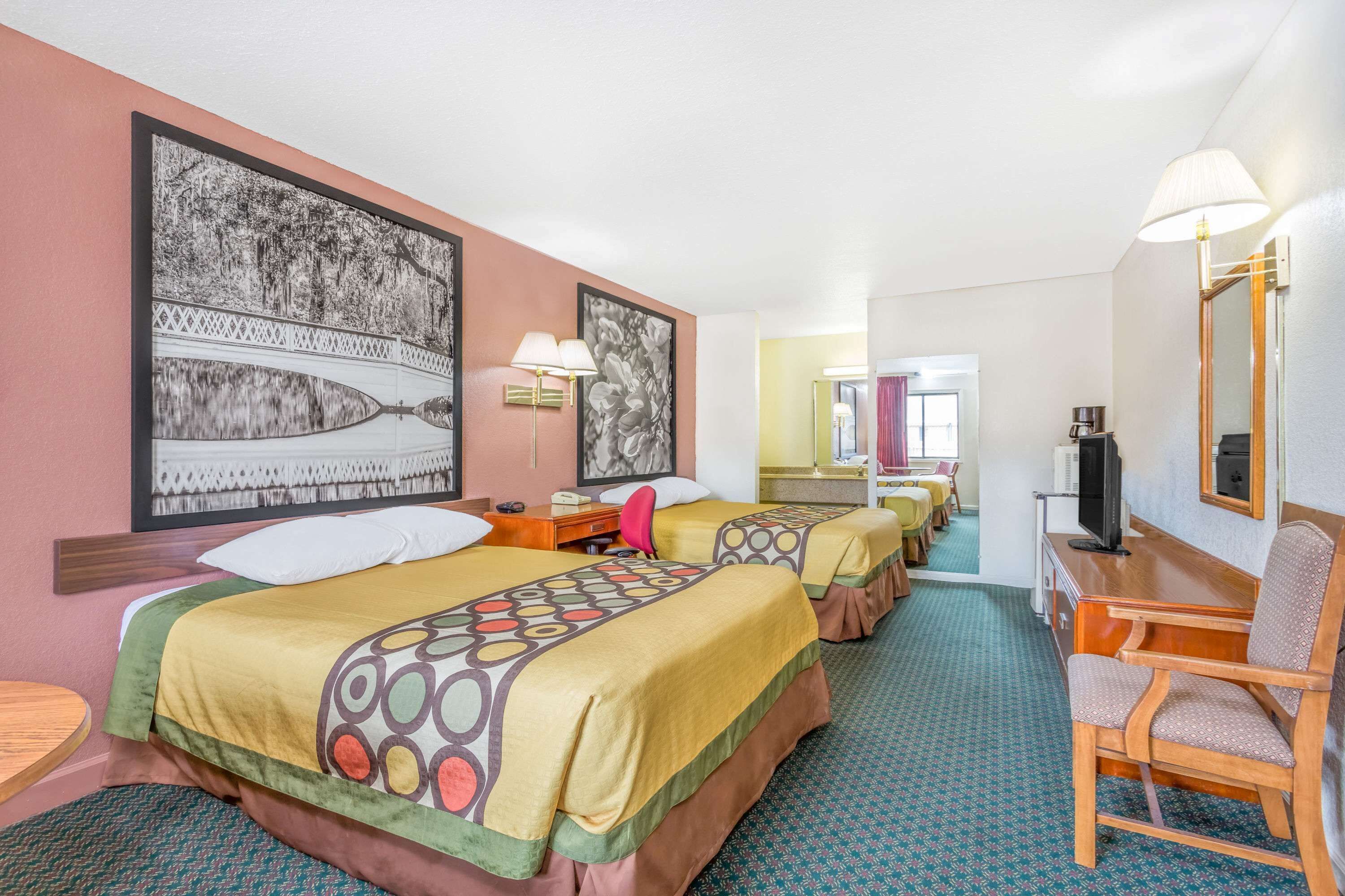 A hotel room with two beds, a desk, a chair, a television, and artwork on the walls.