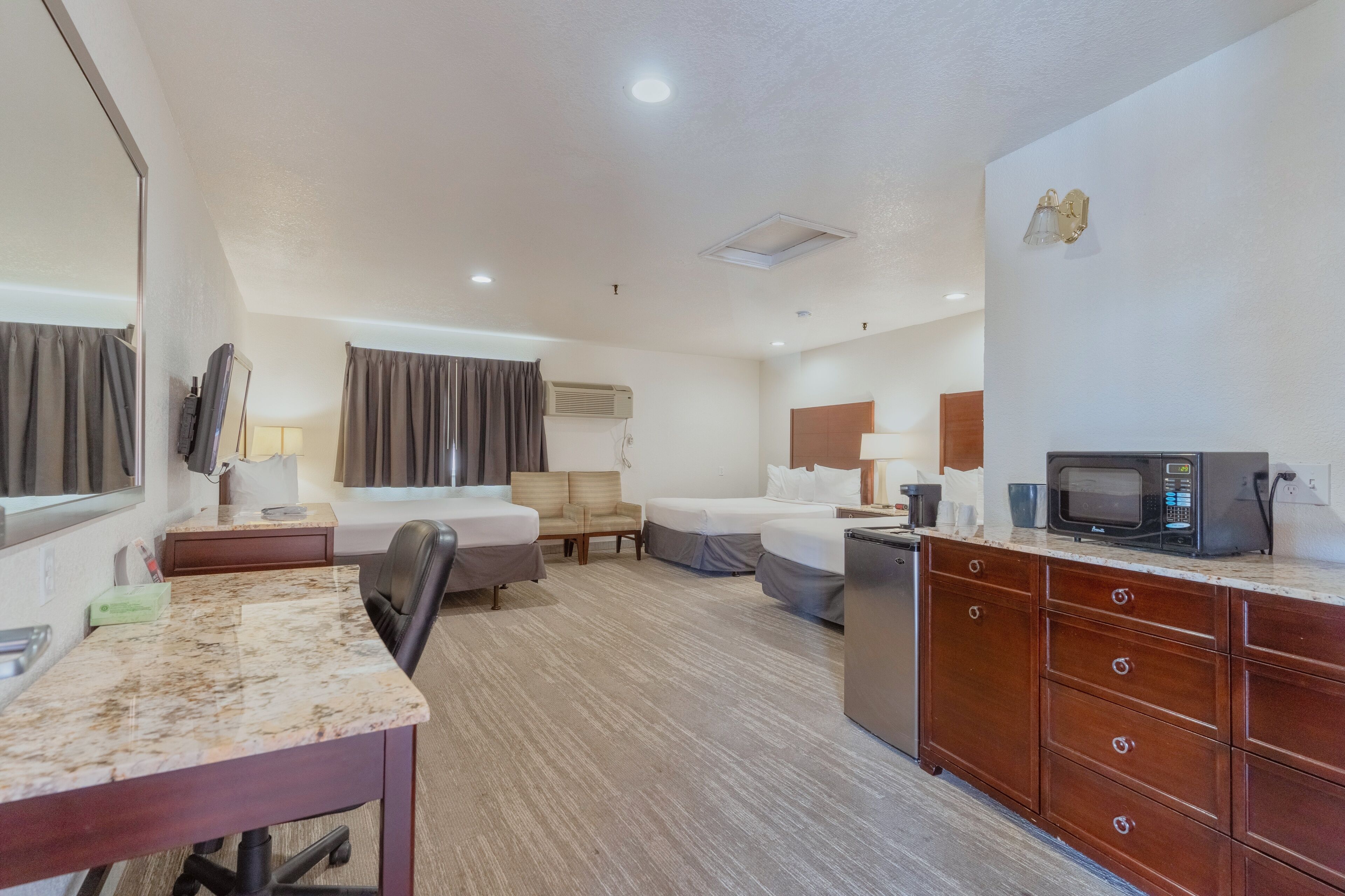 A hotel room with a bed, a desk, a chair, a microwave, and a TV.