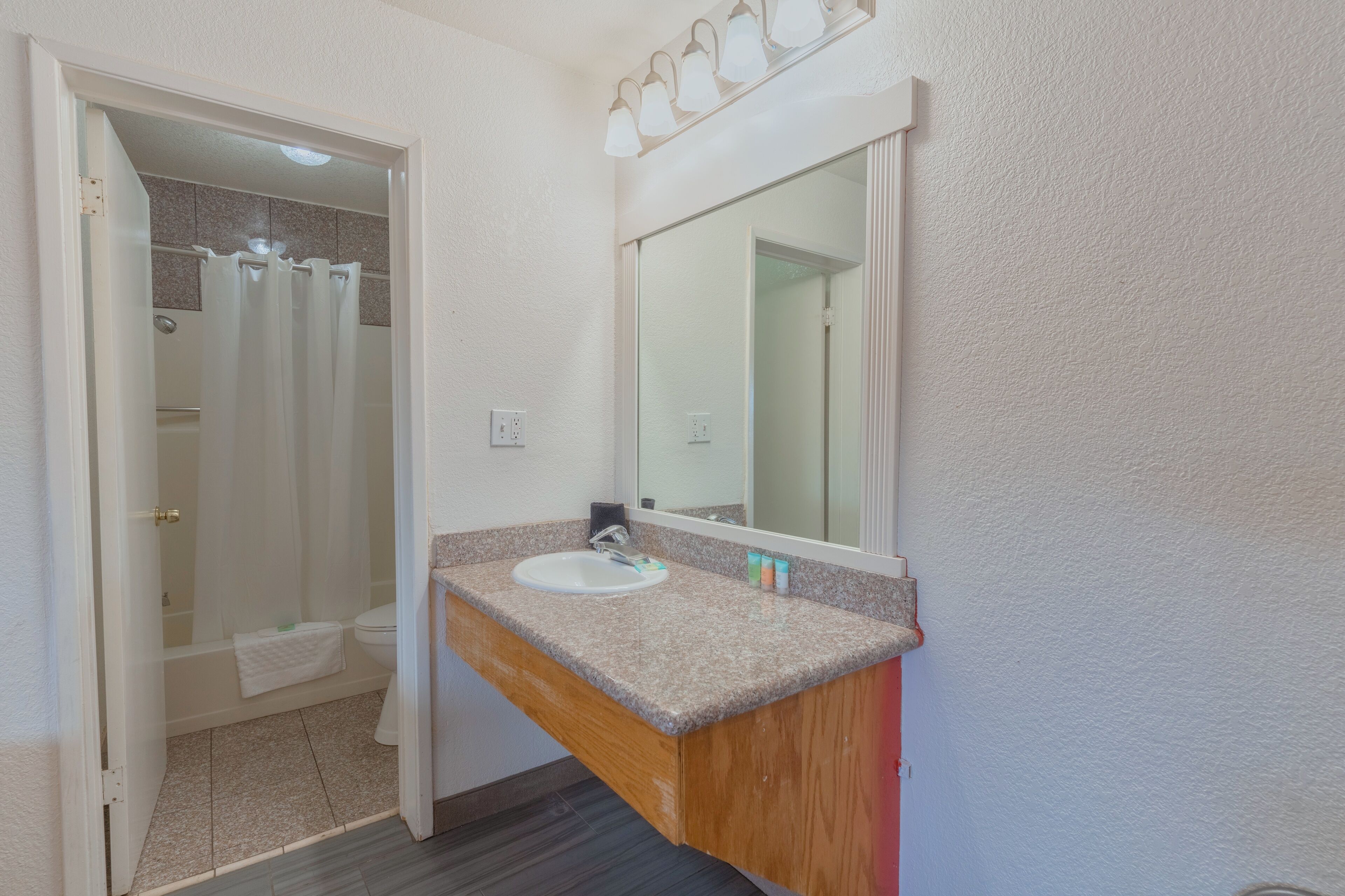Un baño con lavamanos blanco, tocador de madera y un espejo grande.