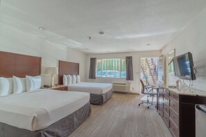 Une chambre d’hôtel avec deux lits, un bureau, une télévision et une fenêtre donnant sur des immeubles et des voitures.