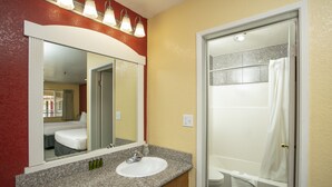 A bathroom with a granite countertop sink, a mirror, and a shower.