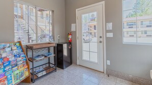Una habitació amb una porta, una finestra, un petit frigorífic i una prestatgeria amb llibres.