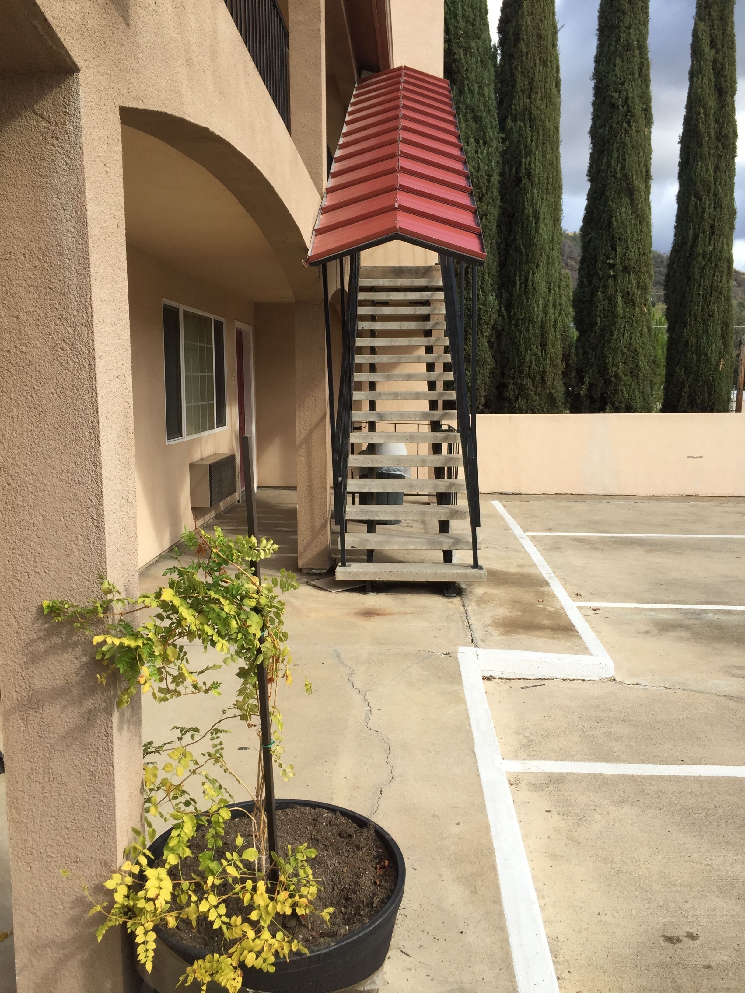 A building with a red-roofed pergola, a small potted plant, and a parking lot.