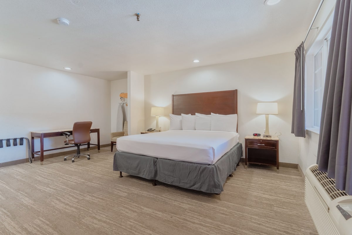 A hotel room with a large bed, a desk, two bedside lamps, and a window with curtains.