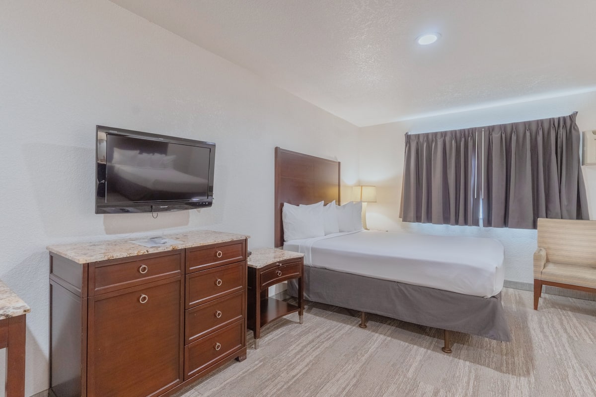 A hotel room with a bed, a TV, a dresser, a chair, and a window with curtains.