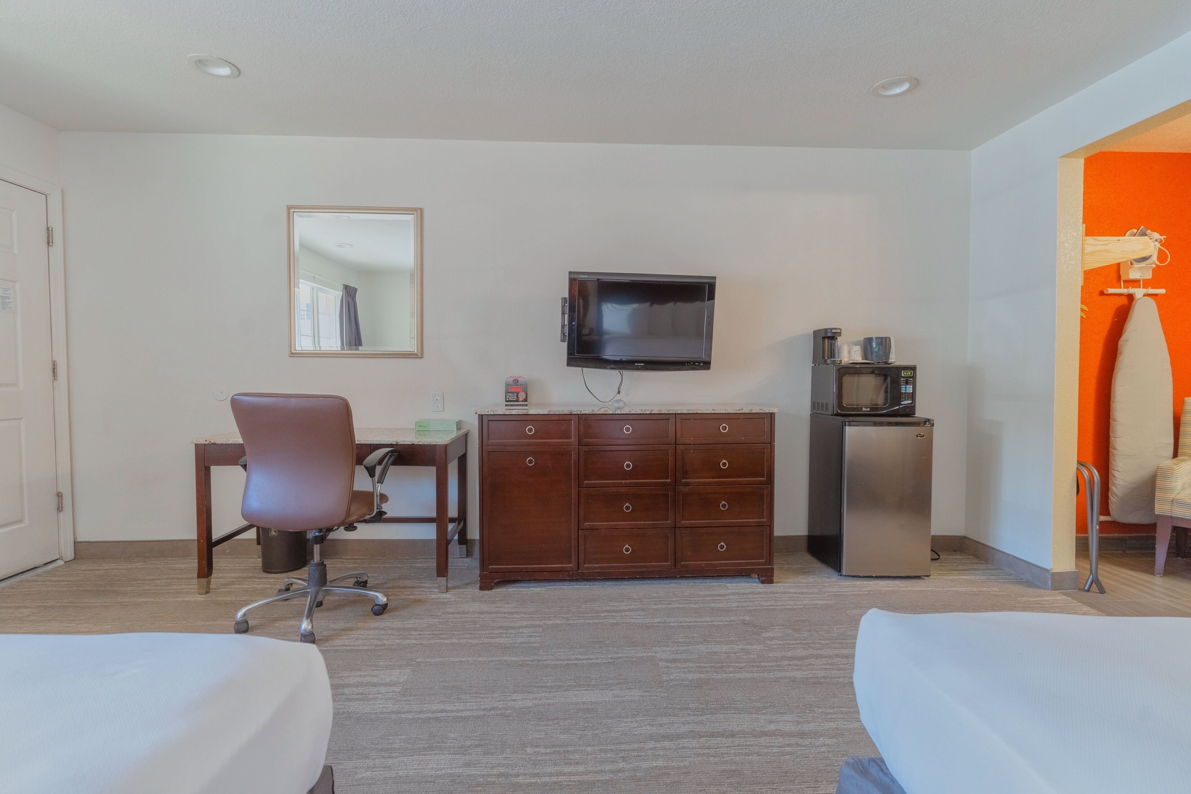 Quarto de hotel com duas camas, uma escrivaninha com cadeira, cômoda, televisão e frigorífico.
