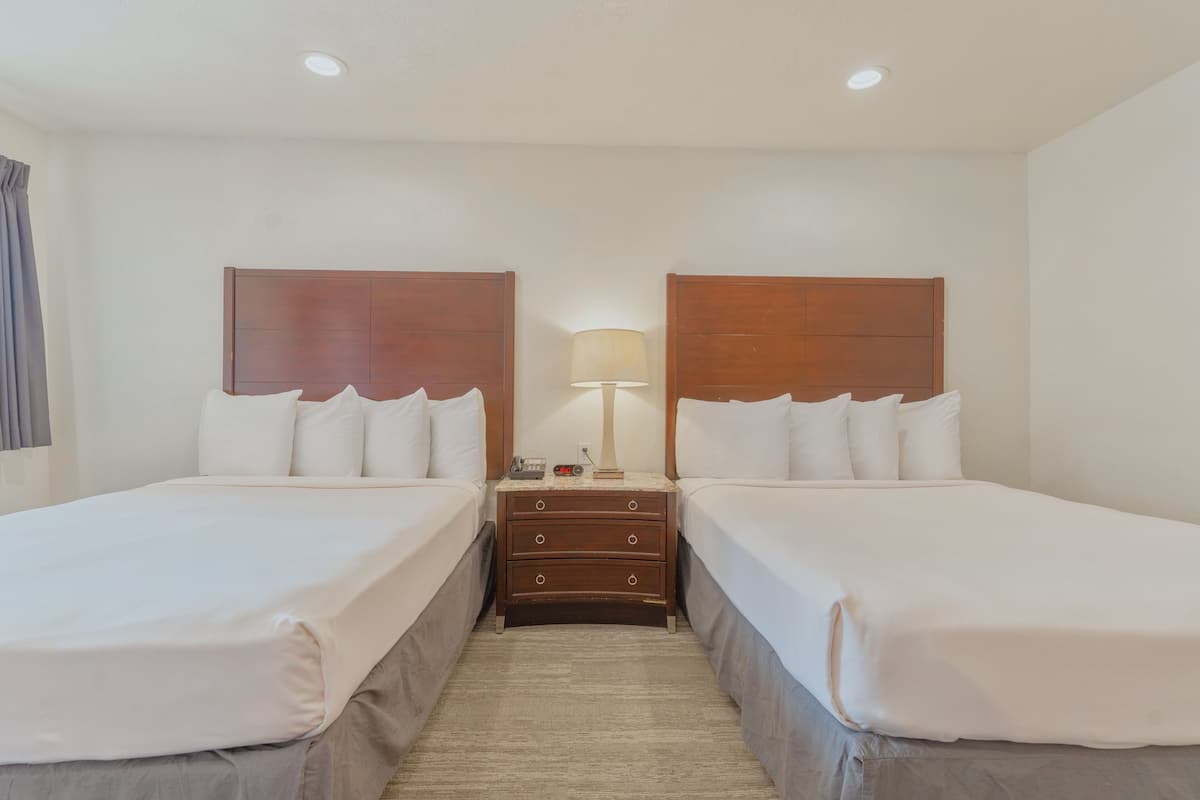 A hotel room with two beds, a nightstand with a lamp, and a small table with a phone and a book.