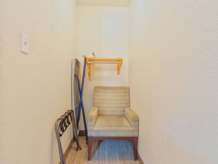 A small, narrow room with a striped armchair, a metal radiator, and a wooden shelf.