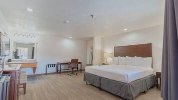 Una habitación de hotel con una cama grande, un escritorio con silla, una tocador con espejo y una lámpara.