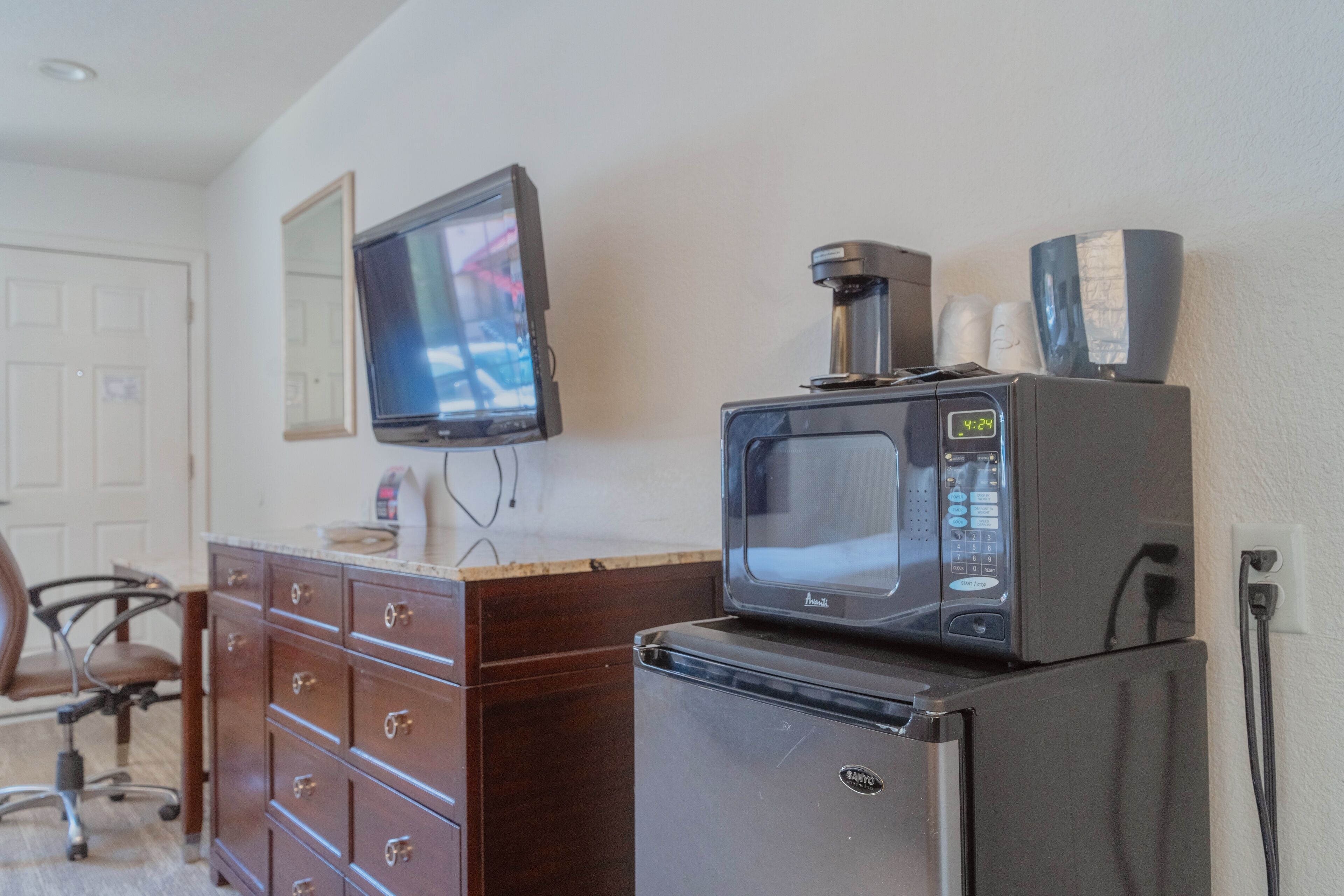 A kitchenette with a microwave, refrigerator, and a television mounted on the wall.