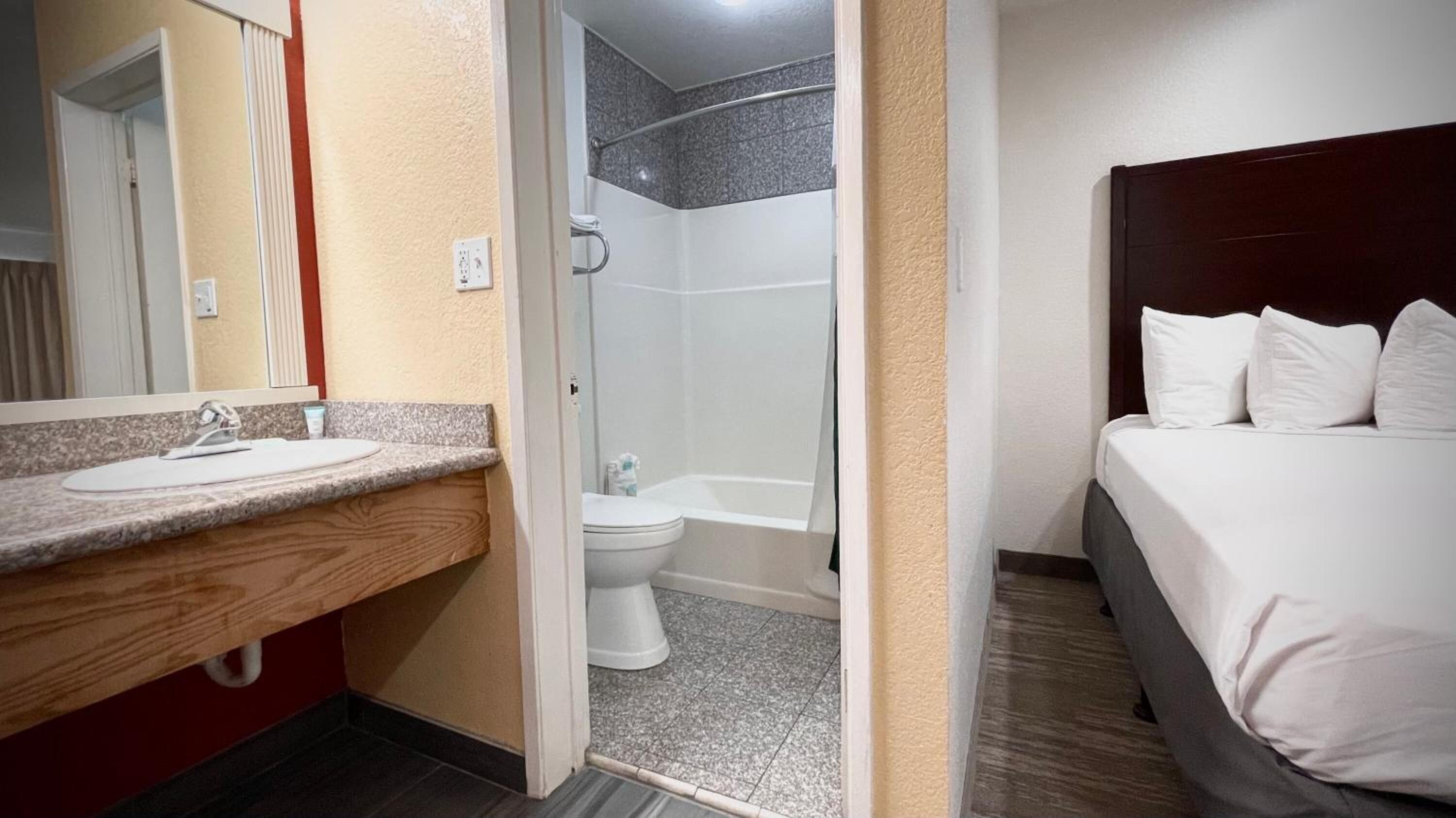 A hotel room with a bathroom that includes a sink, toilet, and shower.