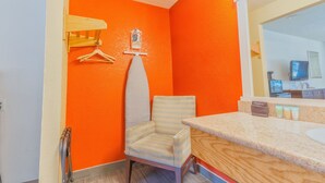 A bathroom with an orange wall, a striped chair, a wooden counter, and a mirror.