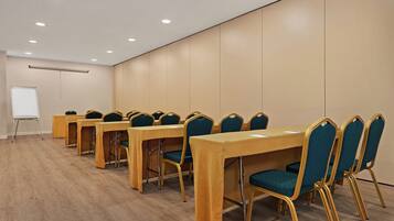 A conference room with long tables and chairs, a whiteboard, and recessed ceiling lights.
