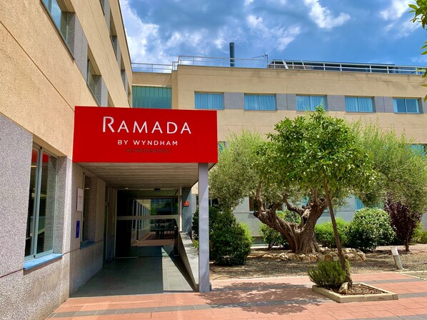 Un edificio con un letrero rojo que dice "RAMADA BY WYNDHAM ALMUSSAFES".