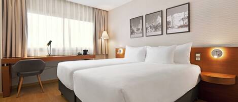 A hotel room with two beds, a desk, a chair, and a large window with curtains.