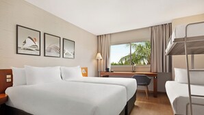A hotel room with two beds, a desk, a chair, a lamp, and a window with a view of palm trees. - Ramada by Wyndham Valencia Almussafes (Almussafes)