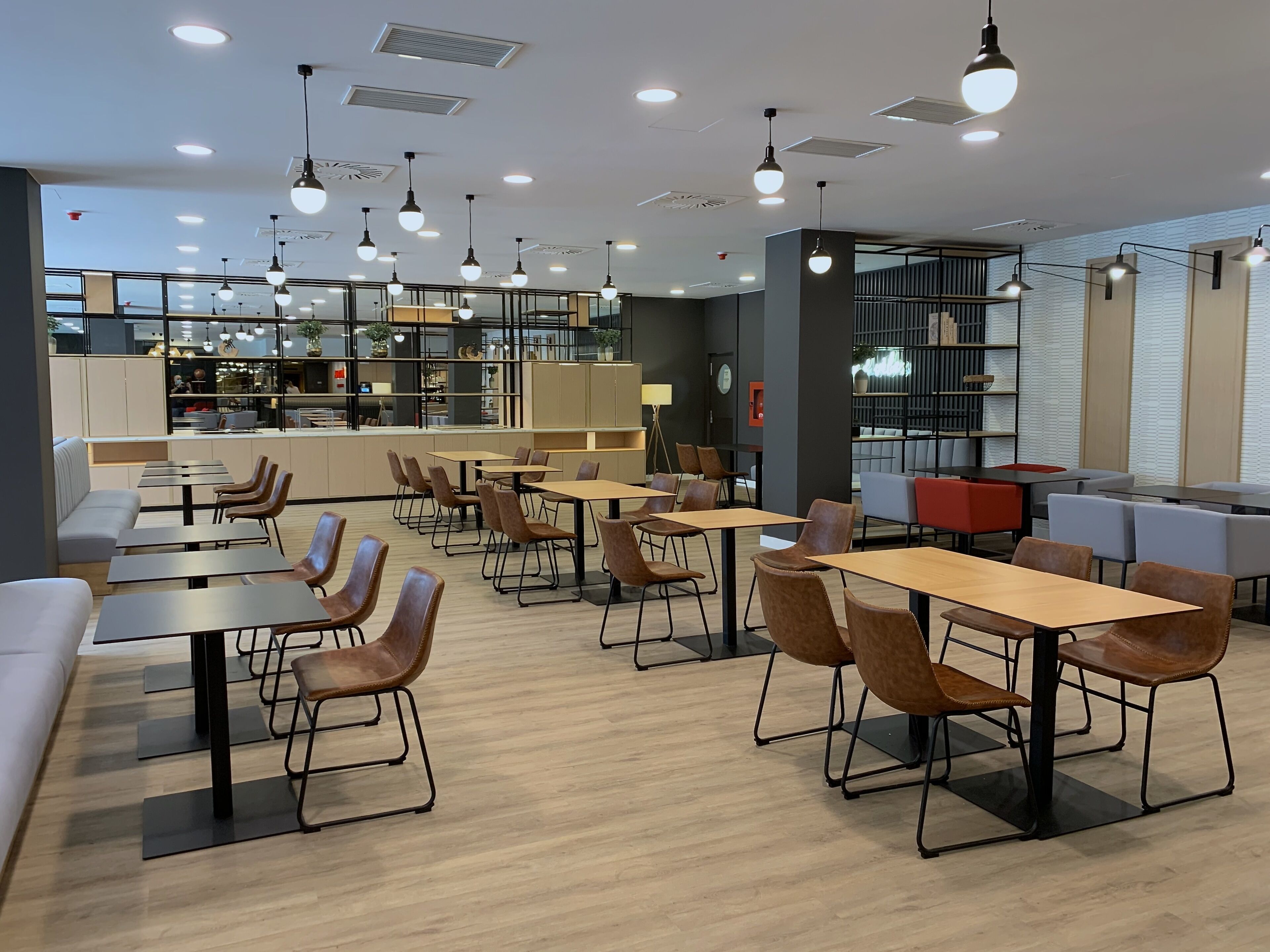 A modern cafe with multiple seating areas, including tables and chairs, and a visible kitchen area in the background.