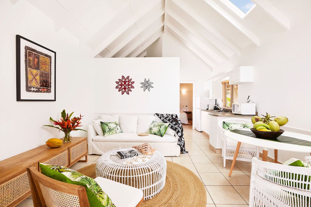 A modern living room with a white sofa, a round wooden coffee table, and a dining area with a white table and wicker chairs.