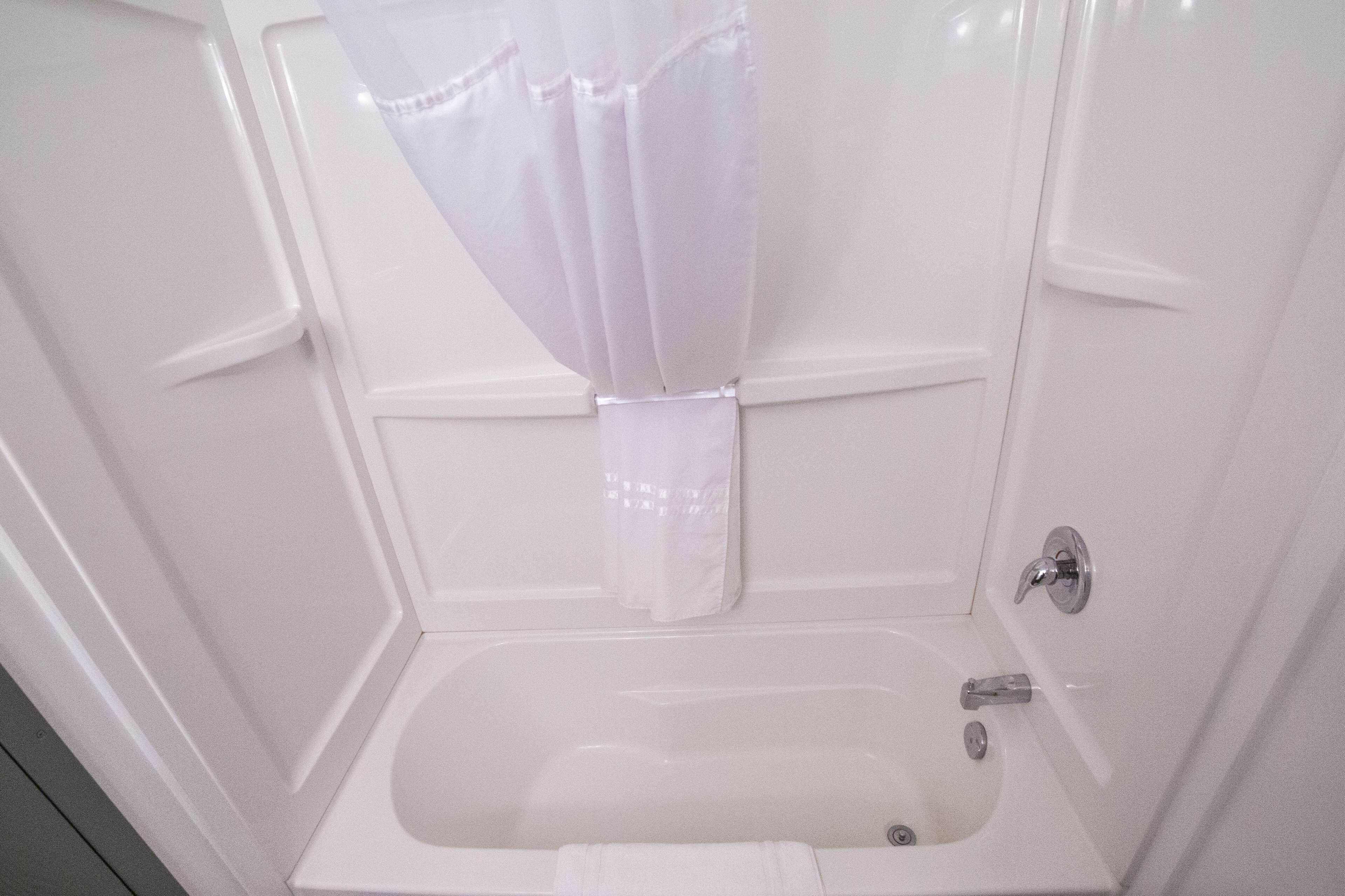 A white bathroom with a bathtub, a shower curtain, and a towel hanging on the wall.