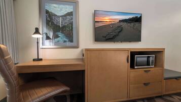 Une chambre d’hôtel avec un bureau en bois, un fauteuil en cuir marron, un tableau représentant un paysage encadré, un téléviseur à écran plat et un four à micro-ondes.