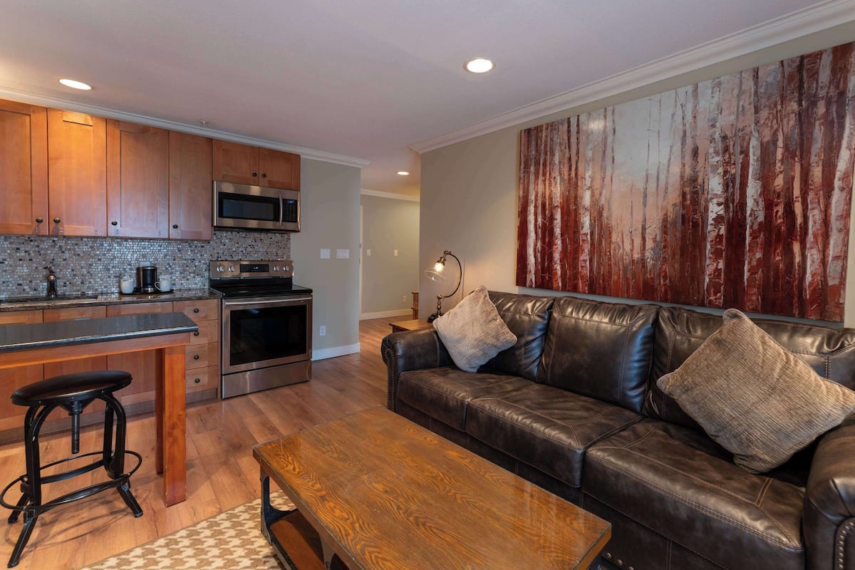 A modern kitchen with stainless steel appliances, a leather sofa, and a wooden coffee table.
