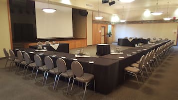 A conference room with a long table, chairs, a projector screen, and a stage area.